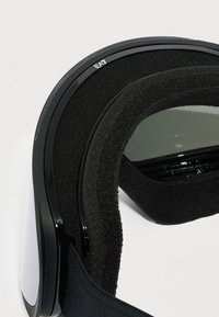 Detailní záběr černých lyžařských brýlí s pěnovým polstrováním a reflexními čočkami na bílém pozadí.