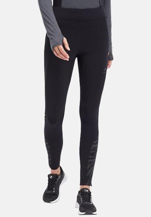 Woman wearing black leggings and black running shoes standing with hands relaxed by sides.