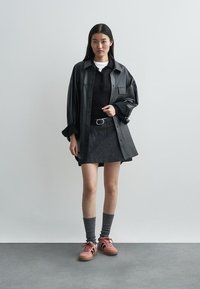 Sobretudo de pele negro, camisola preta justa, saia de ganga escura, meias cinzentas até ao joelho e ténis cor-de-rosa com sola texturada.