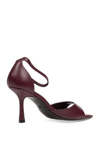 Sandalia de tacón alto de cuero burdeos con correa en el tobillo, punta abierta y tacón de aguja curvado sobre fondo blanco.
