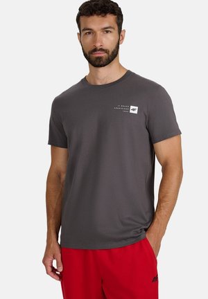 Szara koszulka z krótkim rękawem wykonana z miękkiej tkaniny, z małym białym logo na lewej stronie klatki piersiowej. Gładka tekstura i okrągły dekolt.