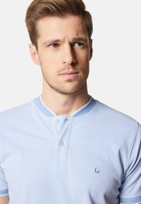 Jasnoniebieska koszulka polo z teksturowanej tkaniny, z guzikami na dwa guziki i kontrastowym kołnierzykiem. Posiada małe ciemnoniebieskie logo na piersi.