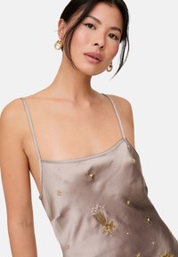 Seiden-Satin-Nachthemd in Taupe mit goldenen, bestickten Sternen und Perlenakzenten, dünnen Trägern und einem lockeren Schnitt. Elegant und mit glatter Textur.