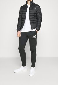 Černá přešívaná péřová bunda, bílé tričko s kulatým výstřihem, černé tepláky s logem a bílé tenisky. Jednoduchý, neformální outfit.