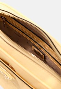 Żółta torebka teksturowana z zapięciem na zamek, z gładką podszewką wewnętrzną i małą metką widoczną w środku.