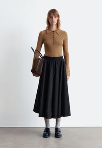 Brown ribbed long-sleeve top with collar and buttons, paired with a black, flowing skirt. Black shoes and gray socks complete the outfit.