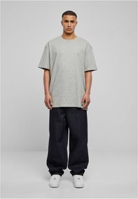 Grå bomulls oversized t-skjorte med kortermede ermer, kombinert med mørkeblå vide jeans og hvite joggesko. Enkelt, uformelt antrekk.