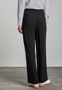 Pantalons larges noirs avec une taille élastique, dotés de deux poches arrière, d'une texture lisse et d'un ourlet soigné. Associés à des baskets blanches.
