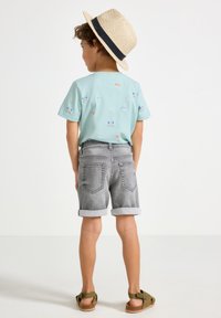 Lyseblå kortærmet t-shirt med farverige krabbe- og fiskemønstre, parret med grå oprullede denimshorts og brune sandaler med stropper.