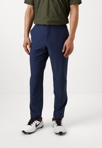 Navy blue pants with a smooth fabric finish, tailored fit, zipper fly, front pockets, and worn with white athletic shoes.