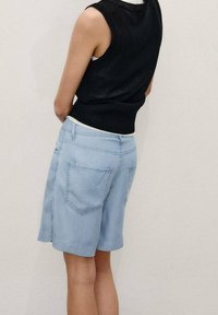 Musta hihaton neulepaita, joka on yhdistetty vaaleansinisiin farkkushortseihin, joissa on takataskut, rento istuvuus ja sileä pinta.