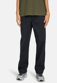 Pantalons noirs à jambe droite en tissu de mélange de coton, avec une coupe décontractée et des poches latérales, associés à des chaussures de sport grises.