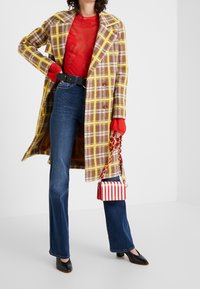 Brown and yellow plaid coat over a red sweater, paired with blue flared jeans and black heels. A small red and white striped handbag completes the look.