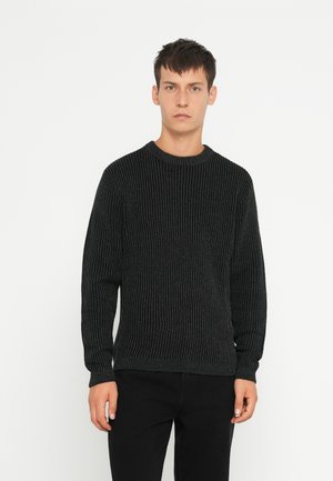 Zwarte gebreide trui met een ronde hals, voorzien van verticale ribbelstructuur en lange mouwen, gecombineerd met donkere broeken.