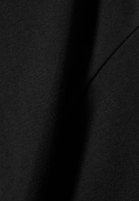 Juoda audinys, turintis minkštą tekstūrą, su raukšlėmis ir subtiliais šviesos kontrastais, išryškinančiais medžiagos pynimą.