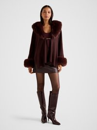 Bordo värvi mahukas kampsun pehme karvase krae ja mansettidega, kombineeritud istuva nahkstega seelikuga ja läikivate põlveni ulatuvate kontsakingadega.