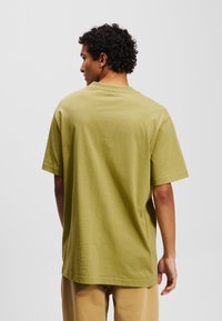 Alyvos žalia medvilninė marškinėliai trumpomis rankovėmis, su apvalia iškirpte ir laisvu siluetu. Lygus paviršius, minimalistinis dizainas, be matomų raštų.