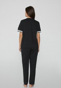 Černý pyžamový set s bílými puntíky, krátké rukávy a krajkový lem na manžetách, obsahuje kalhoty rovného střihu. Měkká látka a volný střih.