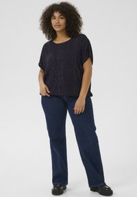 Haut marine à manches courtes avec des rayures verticales argentées, associé à un jean évasé bleu foncé et des chaussures à plateforme noires. Tissu doux, coupe décontractée.
