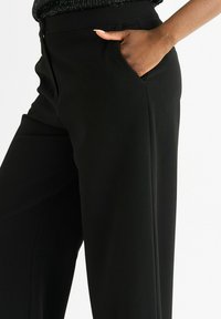 Black wide-leg trousers made from smooth fabric, featuring side pockets and a tailored fit. Clean lines and minimalistic design.