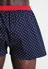 Boxer da uomo blu navy con cintura elastica rossa, caratterizzati da un motivo a stelle bianche. Il tessuto sembra liscio e leggero.