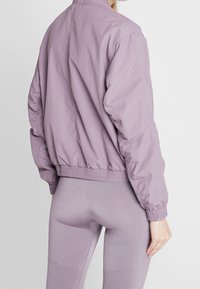 Ljuslila bomberjacka med elastiska ärmslut och nederkant. Har en slät yta och en avslappnad passform. Bärs med matchande leggings.