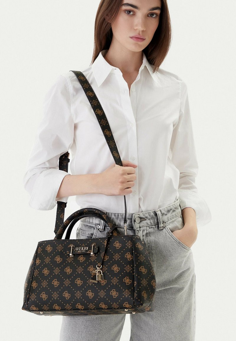 Sac à main noir avec logo à motif doré, forme structurée, double poignée et bandoulière amovible, orné d'un pendentif cadenas doré.