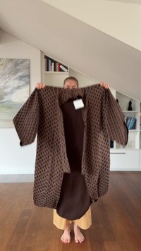 Prenda tipo kimono de color marrón con un patrón, de manga tres cuartos, con el frente abierto y un acabado texturizado. Etiqueta visible, usada sobre un atuendo oscuro.