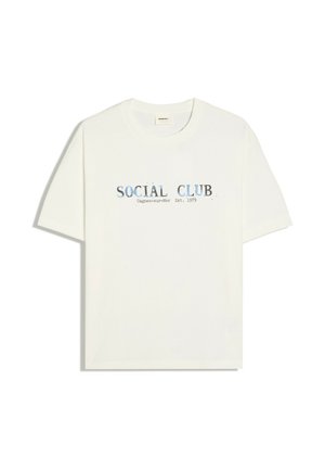 Biele tričko s krátkym rukávom a okrúhlym výstrihom s vyblednutým modrým textom "SOCIAL CLUB Cagnes-sur-Mer Est. 1979" potlačeným na hrudi.