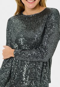 Top de manga larga gris oscuro brillante cubierto de lentejuelas, con un cuello redondo y un corte relajado, con detalles acanalados en los puños.