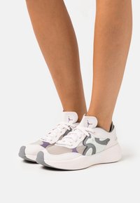 Chaussures de sport blanches avec des accents gris et lavande, dotées d'une tige en maille, d'un système de laçage et d'une semelle en caoutchouc. Conception à bout rond.