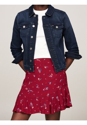 Veste en jean bleu foncé portée sur un haut blanc associée à une jupe rouge à motif floral avec un ourlet volanté.