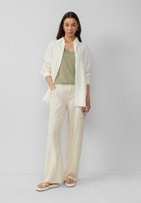 Biała koszula z guzikami, oliwkowy top w serek, kremowe szerokie spodnie z kieszeniami i białe płaskie sandały. Gładkie, lekkie materiały.