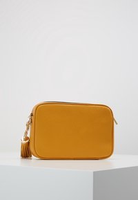 Gul lædertaske med en tekstureret overflade, rektangulær form, hardware i guld-tone og en side-pudse detalje fastgjort til lynlåsen.