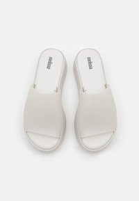 Chanclas blancas de material sintético suave, diseño de punta abierta, forma redondeada y branding minimalista en la plantilla.