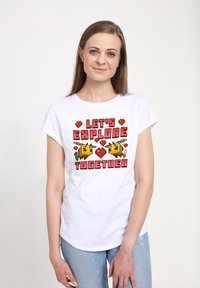 Camiseta blanca de manga corta con un colorido diseño de arte en píxeles que presenta el texto "EXPLORÉMOSLO JUNTOS" y dos abejas amarillas dibujadas con corazones.