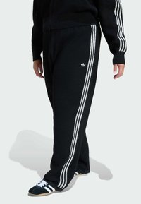 Čierne pletené jogger nohavice s bielymi bočnými pásmi a malým logom. Voľný strih s textúrovanou tkaninou, ktorá má uvoľnenú siluetu.