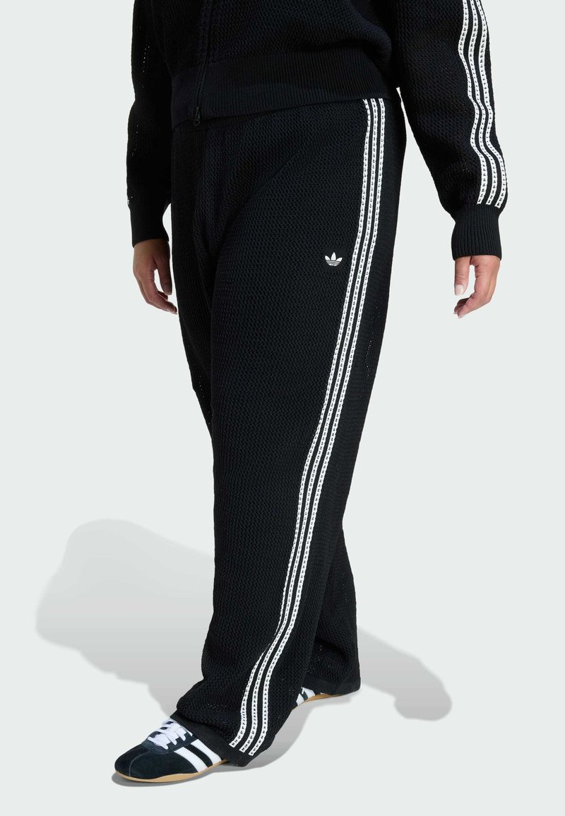 Čierne pletené jogger nohavice s bielymi bočnými pásmi a malým logom. Voľný strih s textúrovanou tkaninou, ktorá má uvoľnenú siluetu.