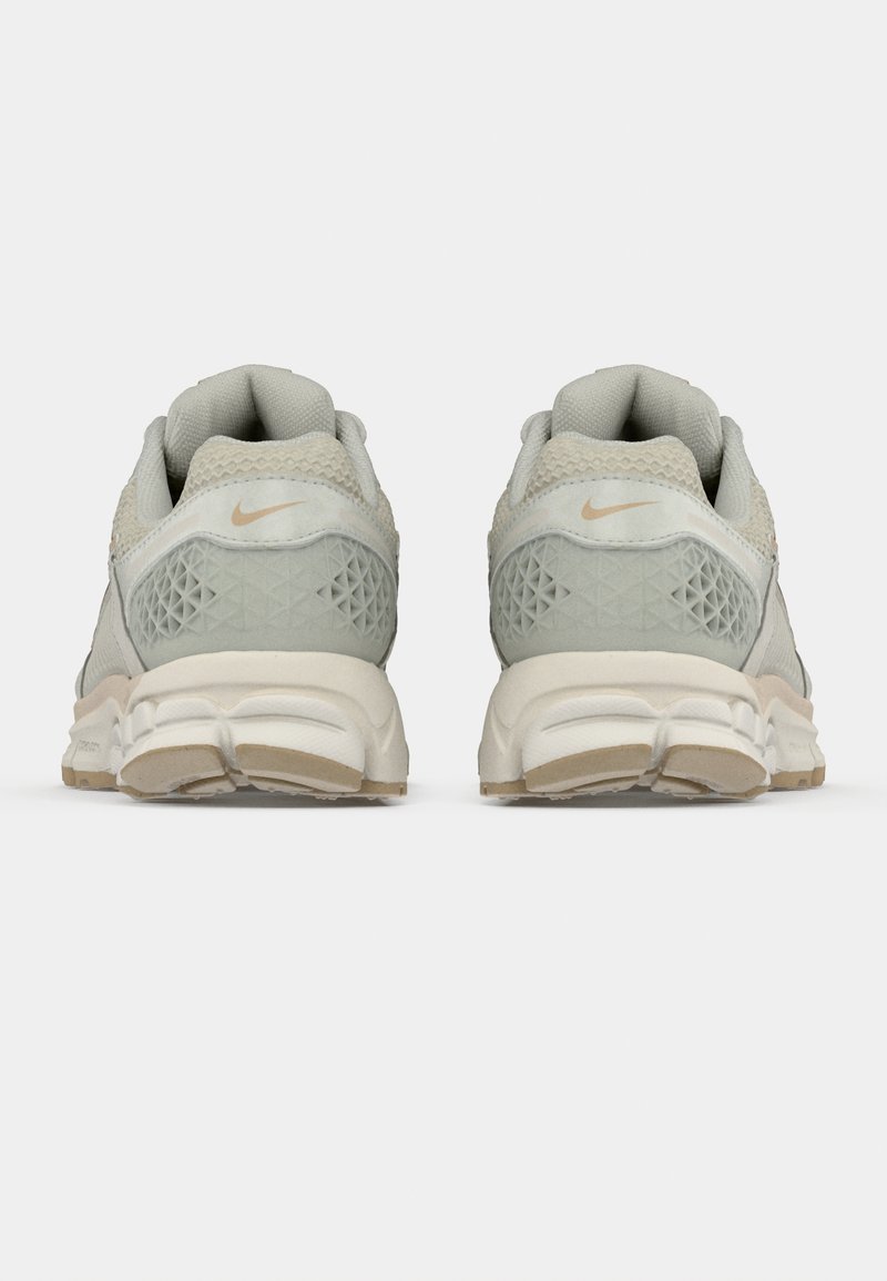 Helle graue Nike-Sneaker mit einem strukturierten Mesh-Obermaterial, das ein Diamantmuster an der Ferse zeigt, sowie einer cremefarbenen Sohle. Sichtbare silberne Akzente.