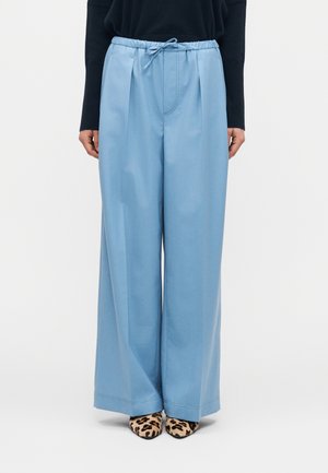 Persona che indossa pantaloni larghi color azzurro chiaro con vita con coulisse, abbinati a una maglia nera e scarpe a punta con stampa leopardata.