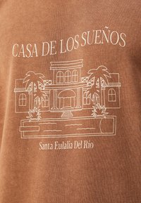 Tessuto marrone con design grafico bianco raffigurante una villa con palme e la scritta "CASA DE LOS SUEÑOS" e "Santa Eulalia Del Río."