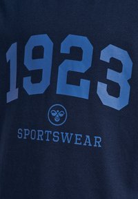 Granatowa koszulka sportowa z dużymi jasnoniebieskimi cyframi "1923" oraz mniejszym niebieskim tekstem "SPORTSWEAR" poniżej.