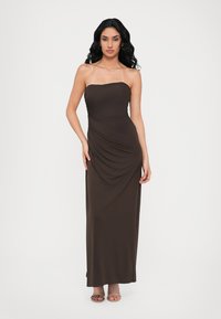 Abito lungo marrone senza spalline realizzato in tessuto morbido con un design drappeggiato su un lato. Presenta un colletto dritto e arriva fino al pavimento.