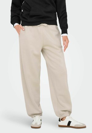 Beige sweatpants with a loose fit, elastic cuffed ankles, and side pockets, paired with a black hoodie and white sneakers.