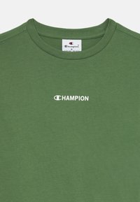 Grønn bomull t-skjorte med rund hals, med en hvit "CHAMPION"-logo trykt på forsiden. Glatt tekstur, minimalistisk design. Størrelse S.