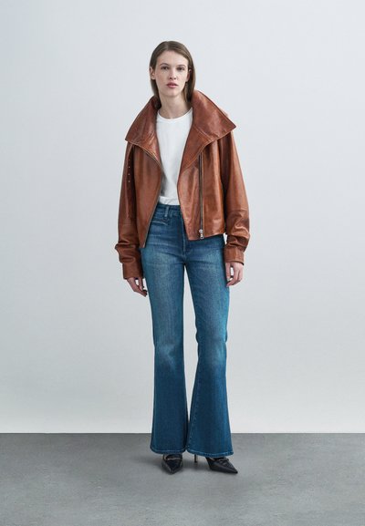 Καφέ δερμάτινο μπουφάν με μεγάλο γιακά, συνδυασμένο με στενά τζιν σε μπλε χρώμα με καμπάνα και μαύρες γόβες με μυτερές μύτες. Απλό λευκό μπλουζάκι από κάτω.