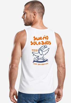 Man with short hair wearing a white tank top with orange and blue toucan surfboard design and text in Spanish and English on the back.