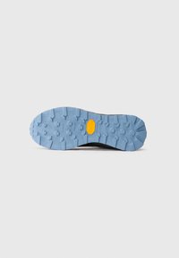 Blauer, strukturierter Gummisohle eines Wanderschuhs mit einem gelben Vibram-Logo in der Mitte, auf einem schlichten weißen Hintergrund dargestellt.