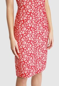 Rotes Spitzenkleid mit floralem Muster, taillierter Silhouette, knielangem Schnitt und kontrastierendem weißen Futter unter der Spitze.
