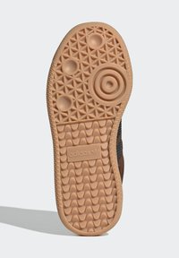 Brauner Gummisohle eines Turnschuhs mit einem strukturierten Grip-Muster, das kreisförmige und sternförmige Akzente aufweist. Adidas-Logo auf der Seite geprägt.